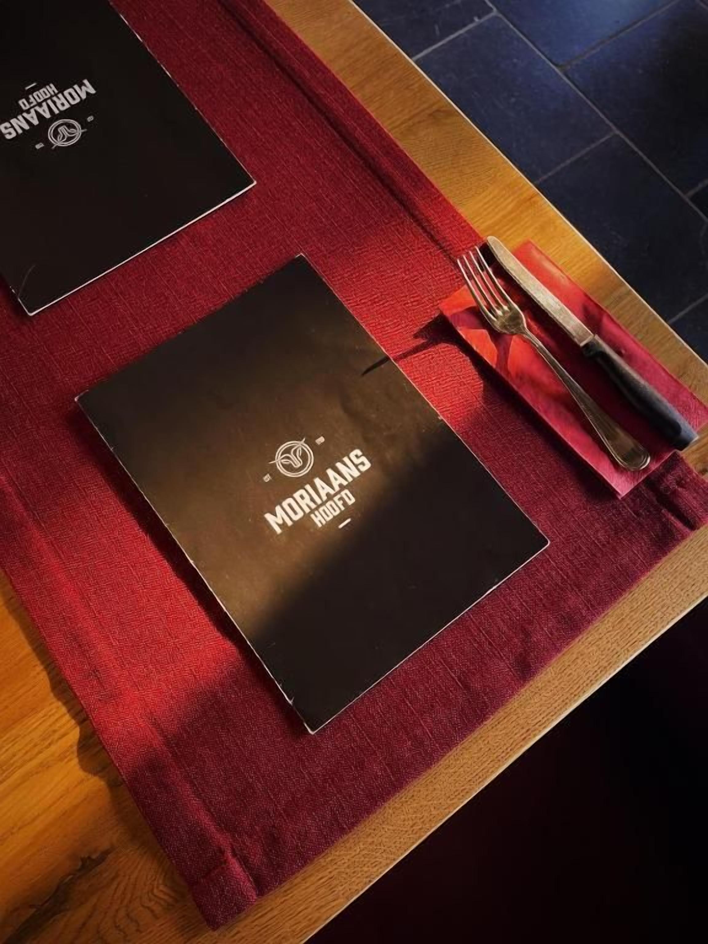 A table with two black folders and a red napkin with a fork and knife on it.