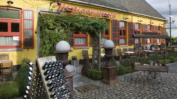 A yellow building with a sign reading "Moraanshouwd". There are outdoor tables and chairs, and a display of wine bottles.