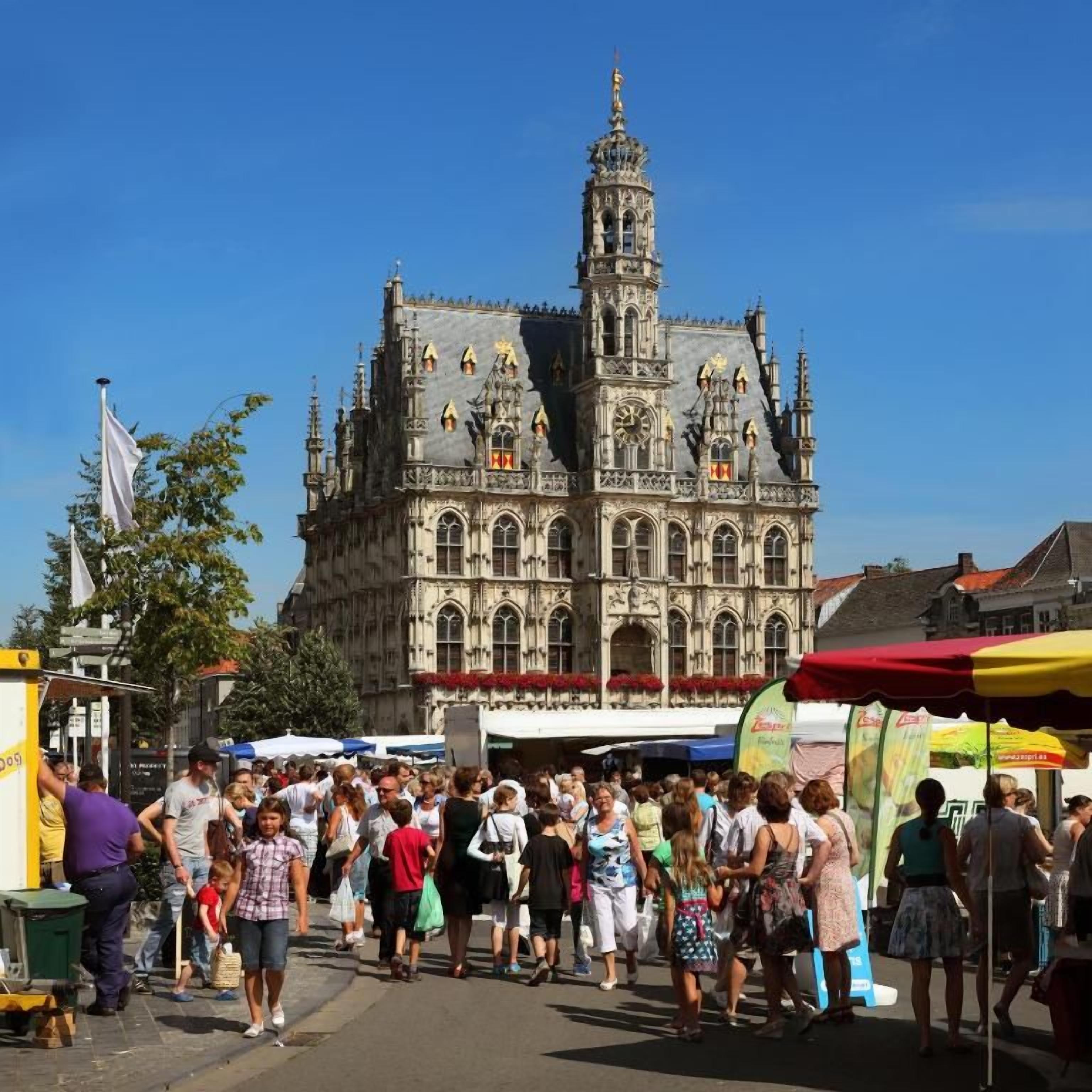 Un bâtiment historique à l’architecture complexe, une foule de personnes et des étals de marché.