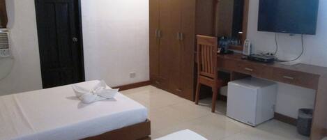 A hotel room with two beds, a desk, a chair, a television, and a small refrigerator.
