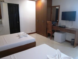 A hotel room with two beds, a desk, a chair, a television, and a small refrigerator.
