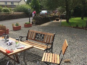 A wooden bench and table with scattered items, surrounded by gravel and potted plants. - Barton Gate Farm Guesthouse (Holsworthy)
