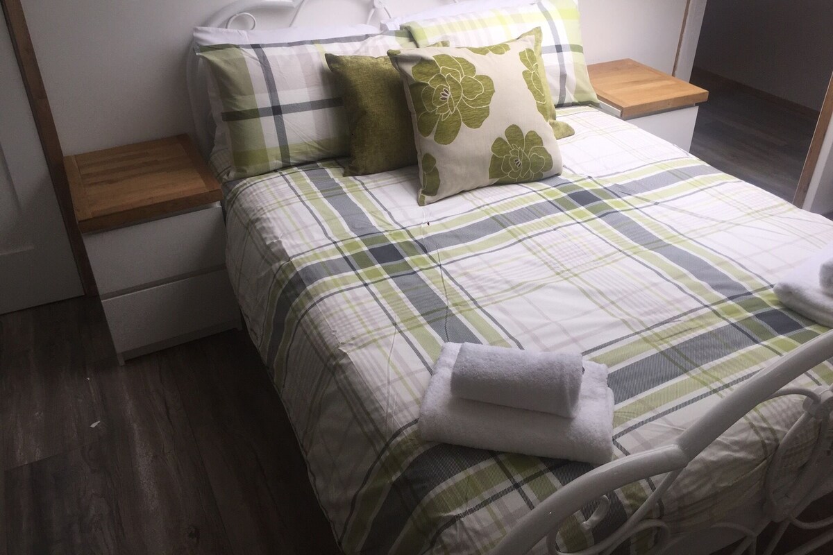 A neatly made bed with a plaid bedspread, two pillows, and a folded towel.