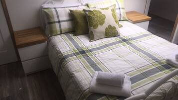 Una cama bien hecha con una colcha escocesa, dos almohadas y una toalla doblada.