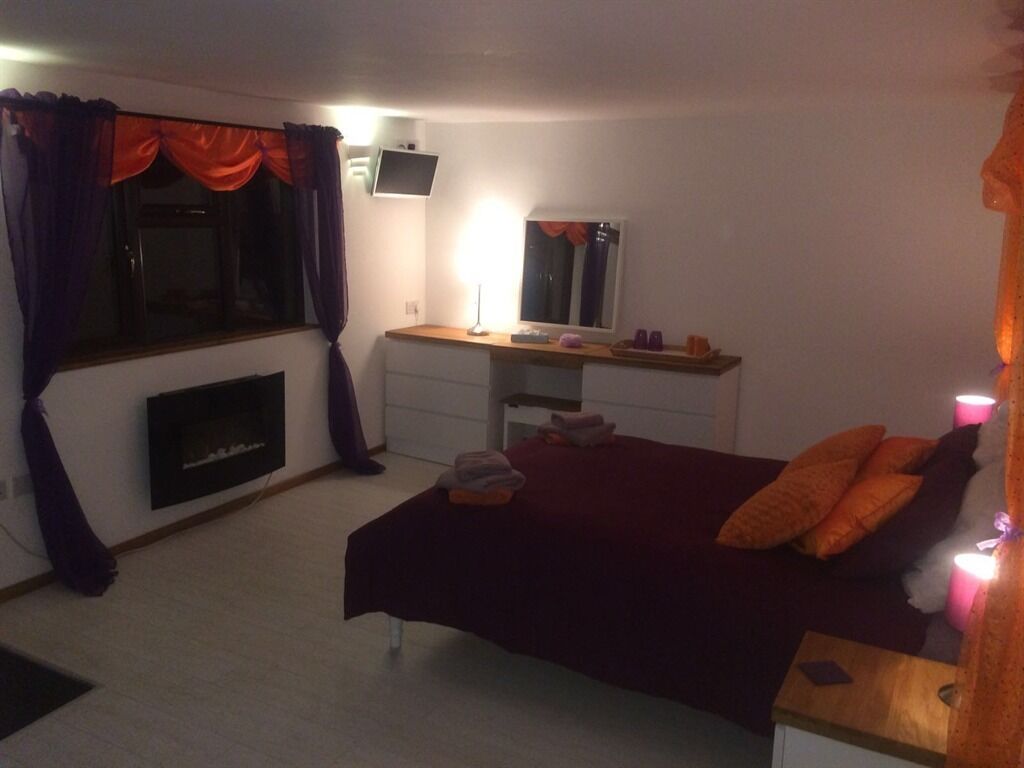 A bedroom with a bed, a desk, a mirror, a fireplace, and a window with curtains.