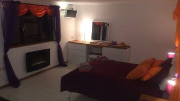 A bedroom with a bed, a desk, a mirror, a fireplace, and a window with curtains.