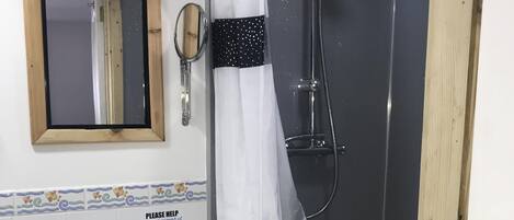 Un baño con ducha, lavamanos, espejo y una botella de gel hidroalcohólico.