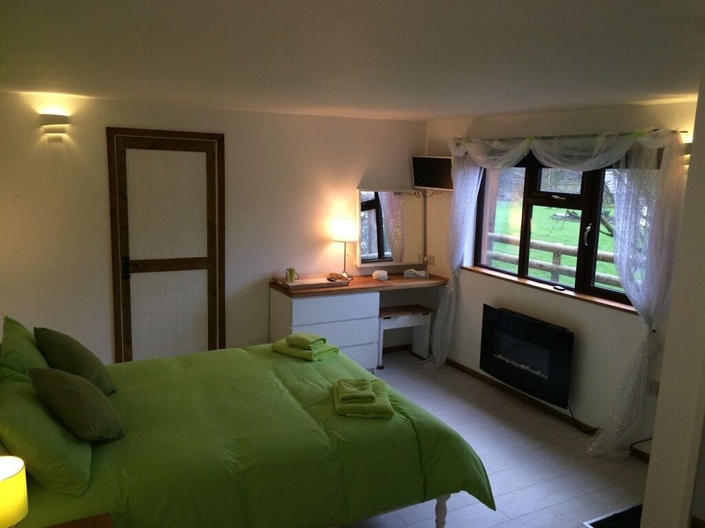 A bedroom with a bed, a desk, a TV, and a window with curtains.
