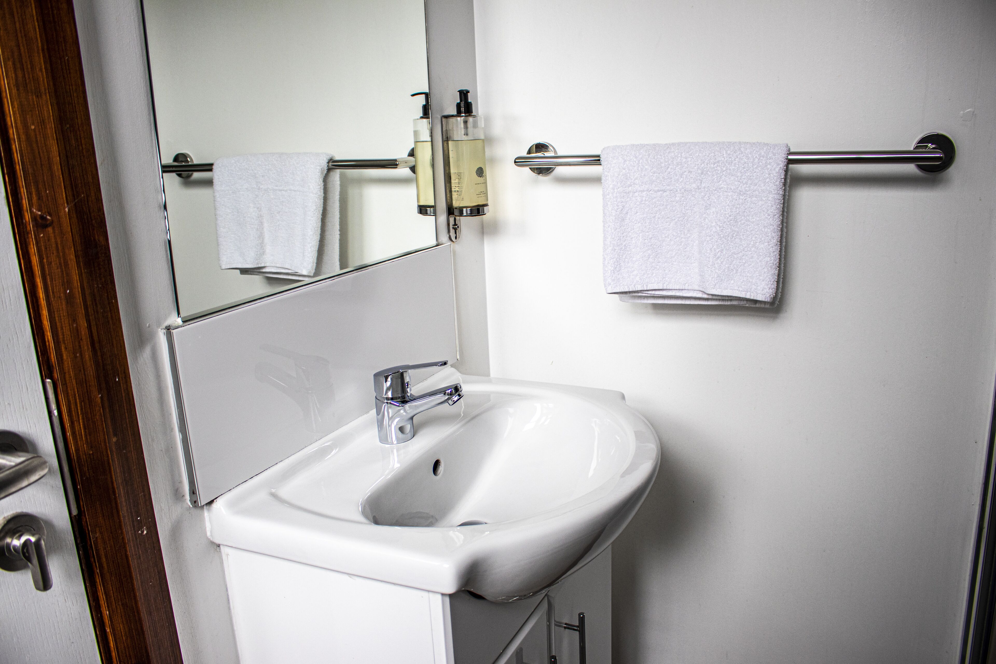 A bathroom with a white sink, a mirror, and two towels hanging on a towel bar.