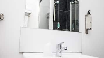 Une salle de bain moderne avec un lavabo blanc, un grand miroir et une douche à parois de verre.