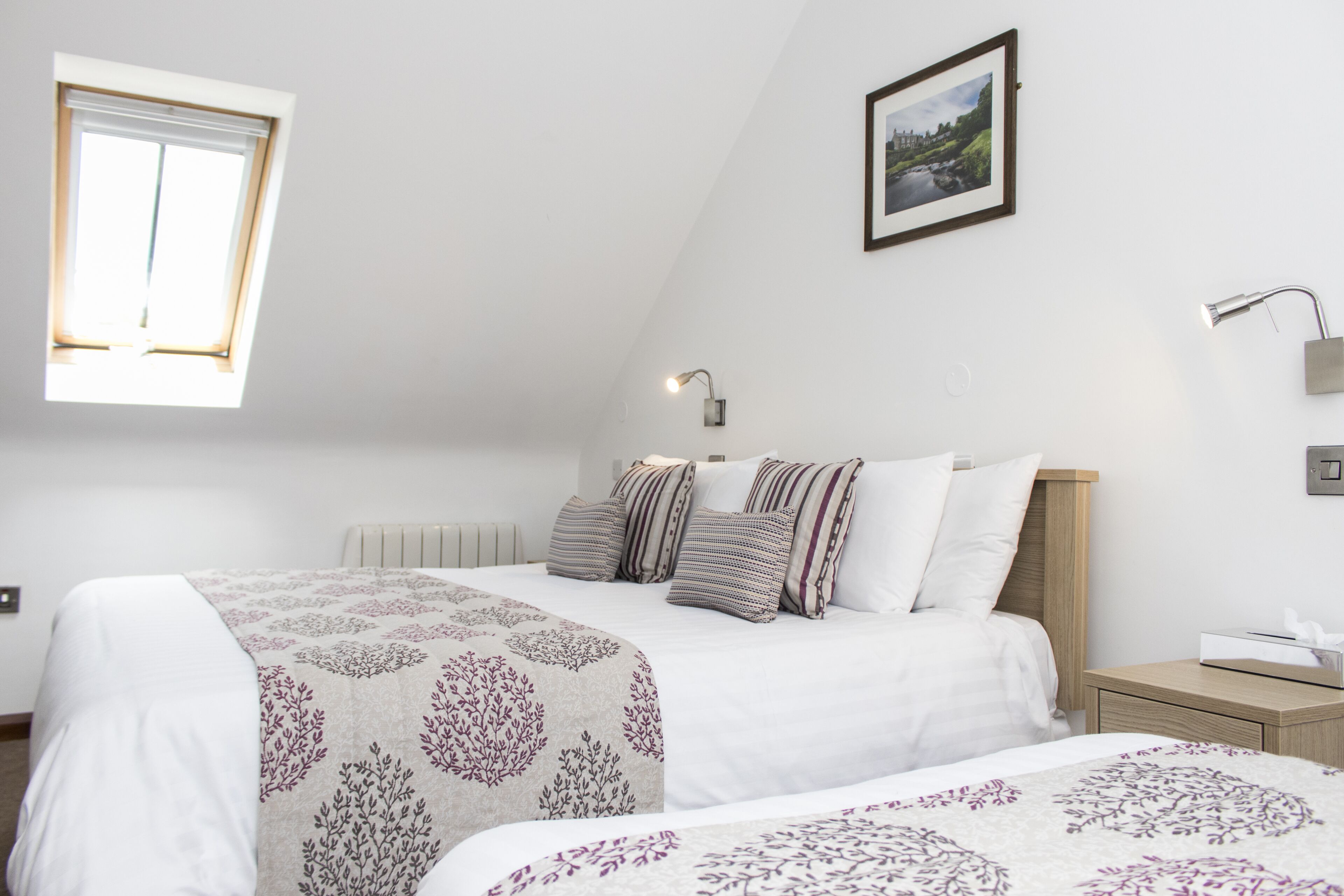 Quarto com cama, mesa de cabeceira, luminária, janela e quadro na parede.