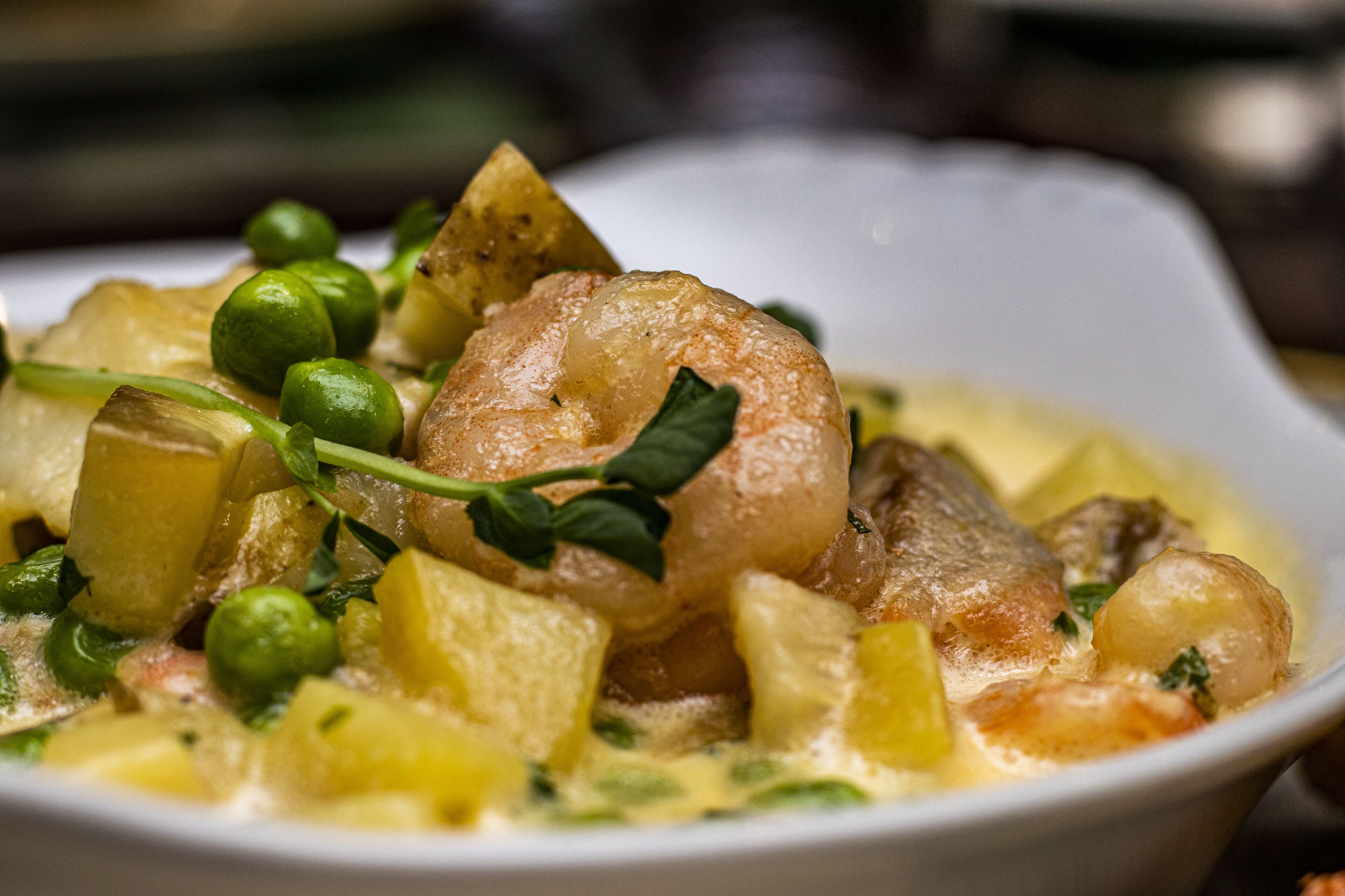 A bowl of seafood stew with shrimp, potatoes, and peas.