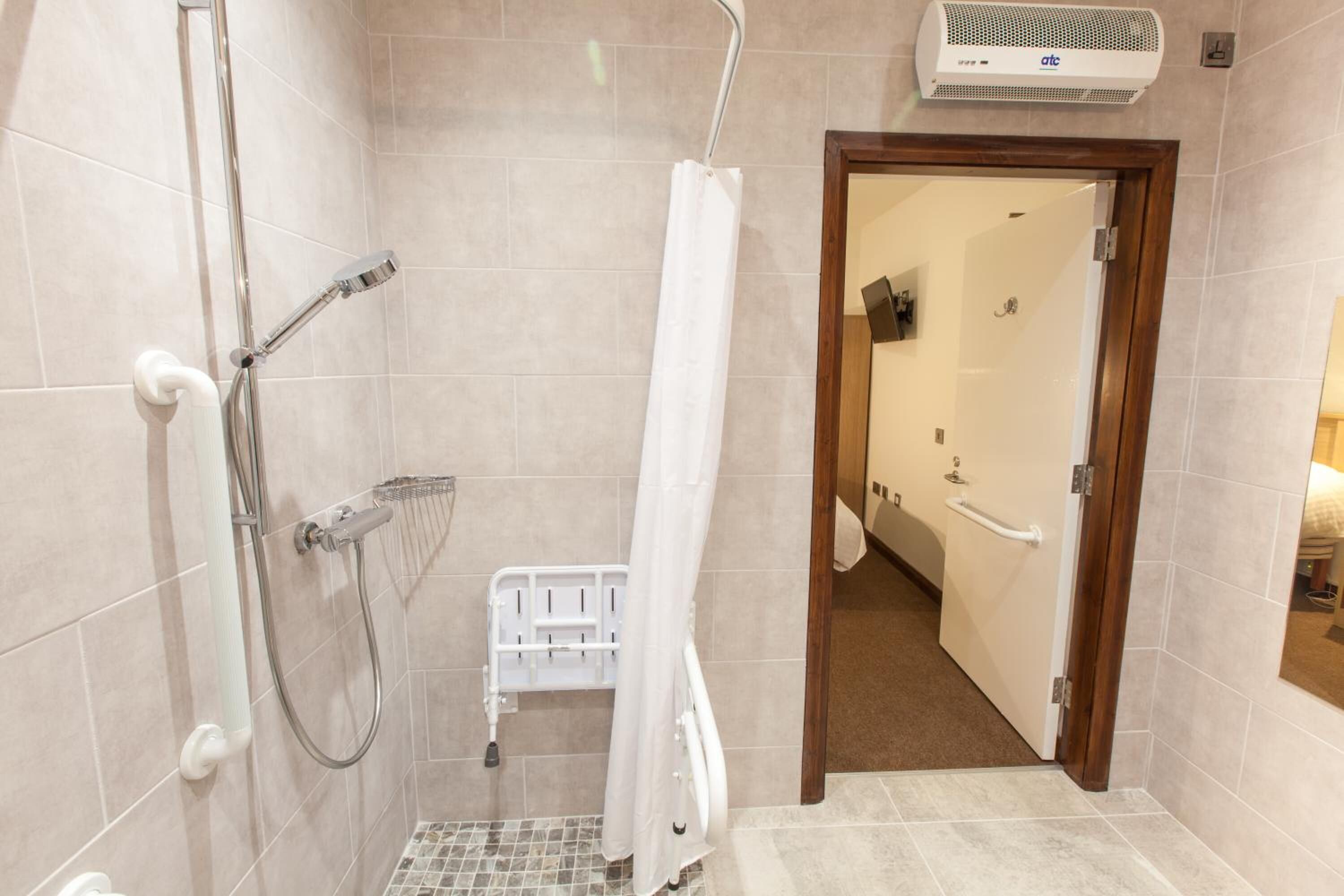 A shower with a handheld showerhead, a white shower curtain, and a white grab bar.