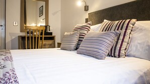 A neatly made bed with striped pillows, a bedside table with a lamp, and a mirror on the wall. - The Rostrevor Inn (Newry)