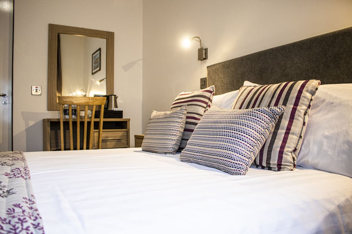 A neatly made bed with striped pillows, a bedside table with a lamp, and a mirror on the wall.