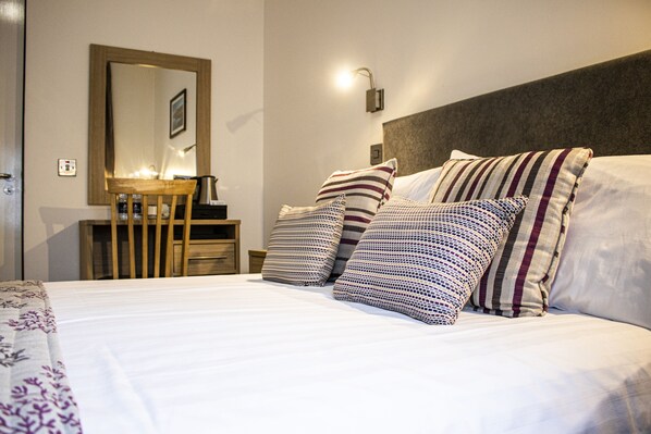 A neatly made bed with striped pillows, a bedside table with a lamp, and a mirror on the wall.