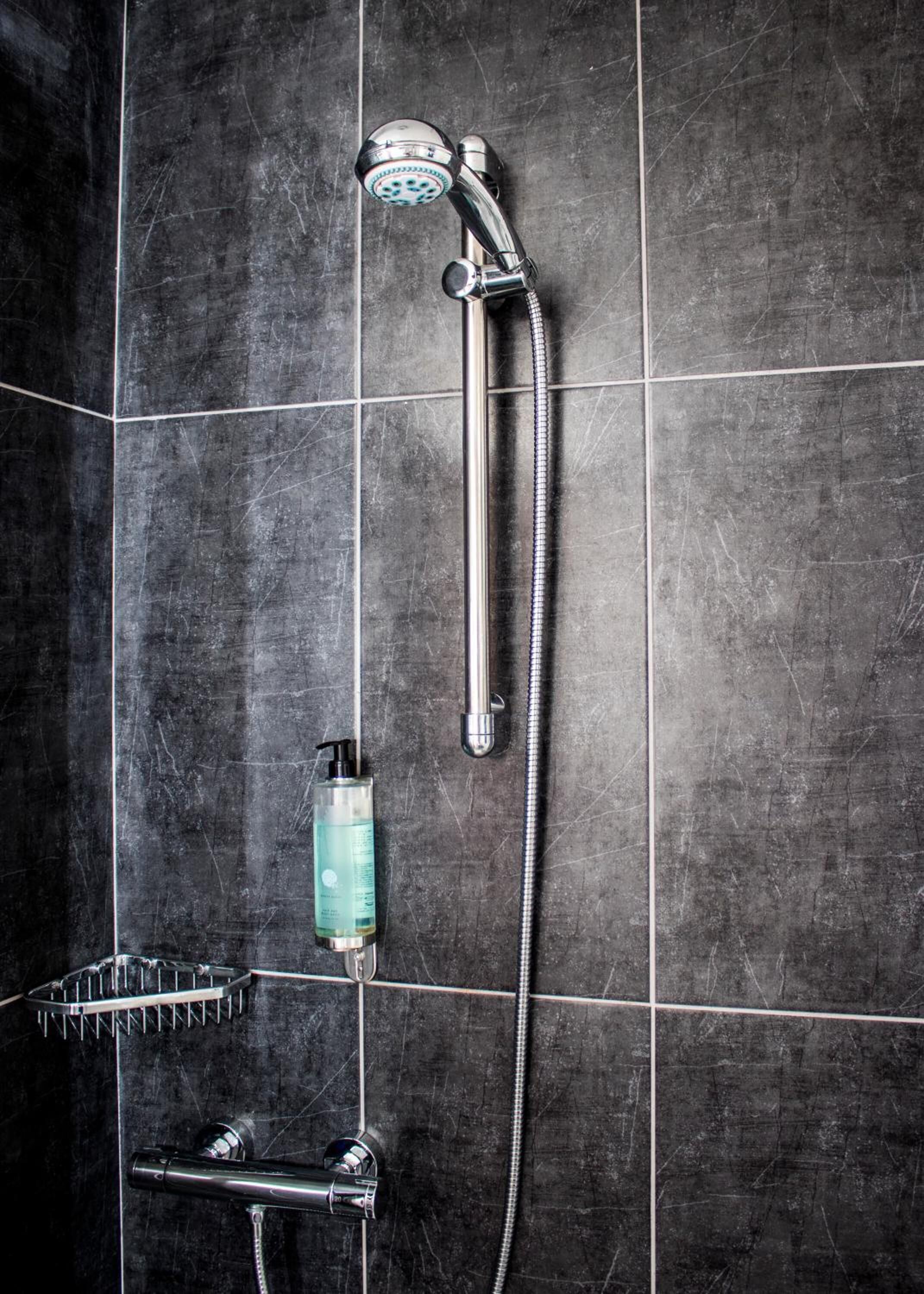 A shower with a handheld showerhead, a handheld shower attachment, and a handheld shower hose.