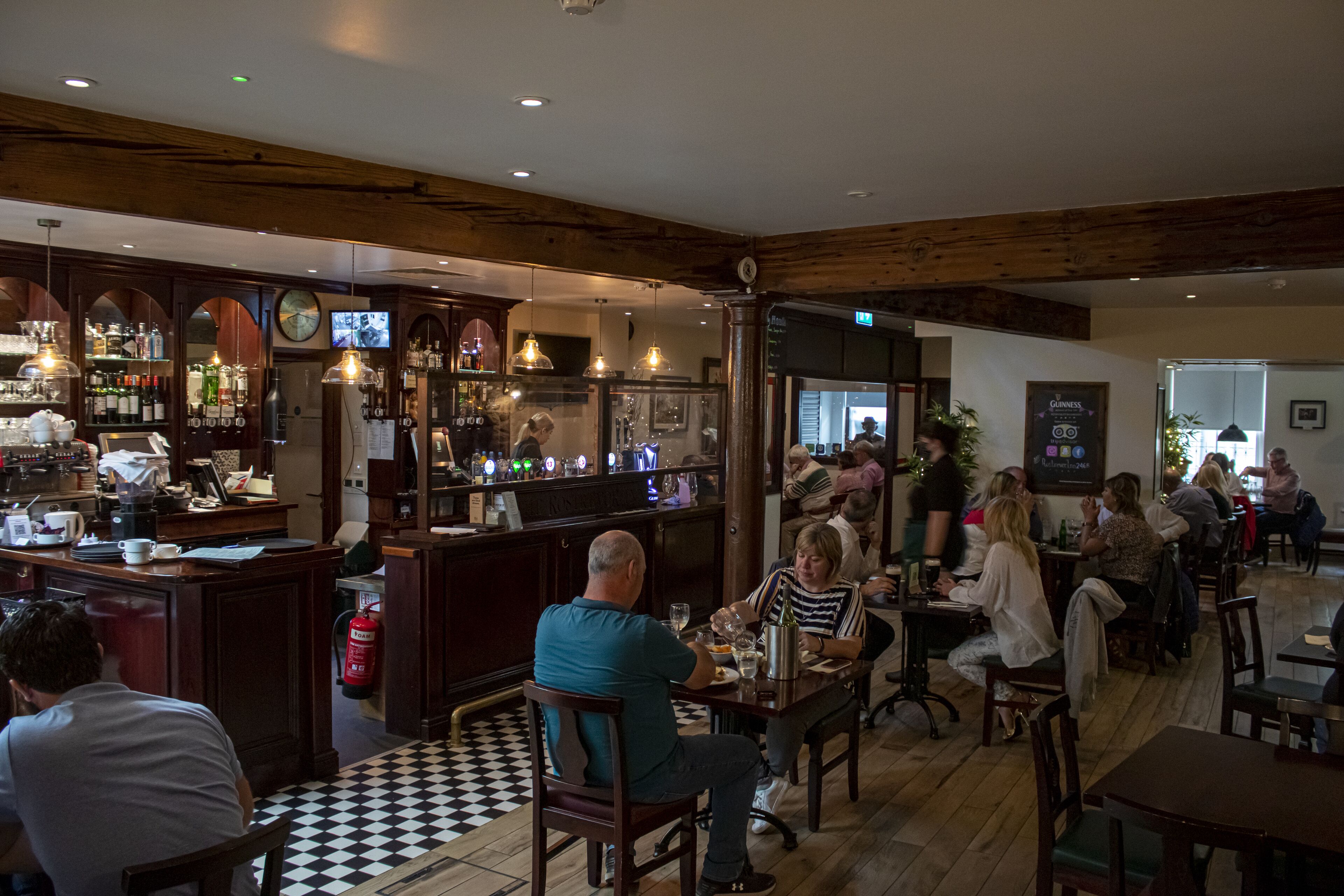 Un restaurante con vigas de madera, una zona de bar y comensales.