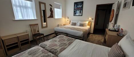 Habitación de hotel con dos camas, un escritorio, una silla, un espejo y una puerta que da a otra habitación.