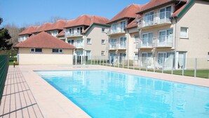 A swimming pool with a tiled deck, surrounded by multi-story buildings with balconies. - Holiday Suites De Haan (De Haan)