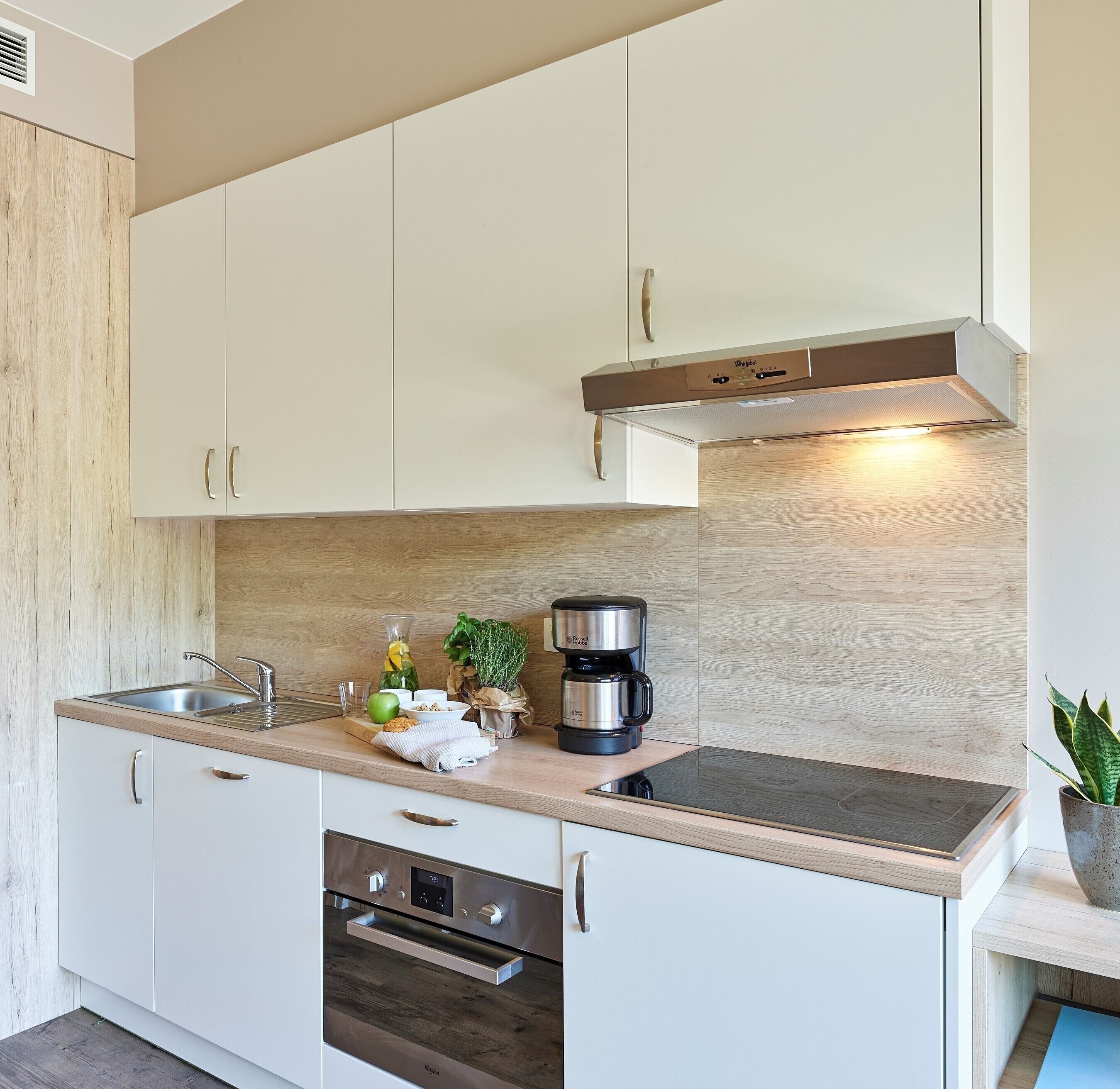 A modern kitchen with white cabinets, a stainless steel range hood, a built-in oven, and a coffee maker on the countertop.