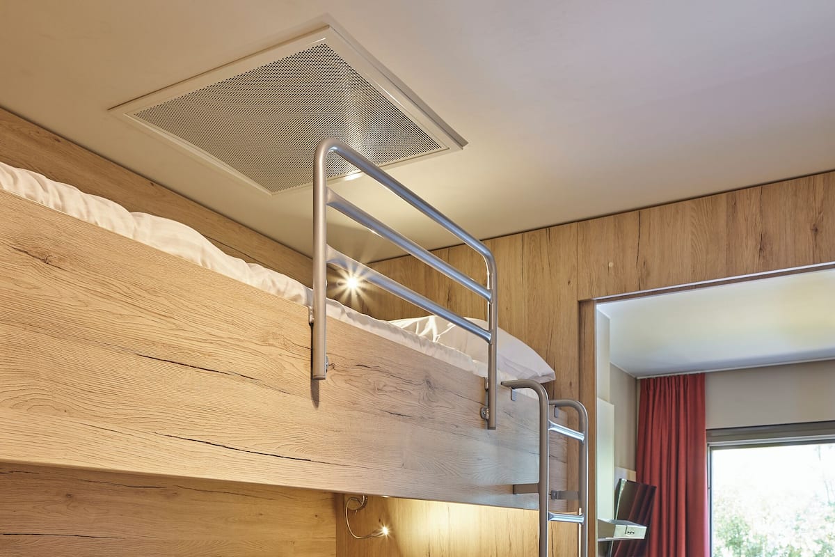 Une chambre avec un lit superposé, une tête de lit en bois, une échelle et un petit bureau avec une chaise.