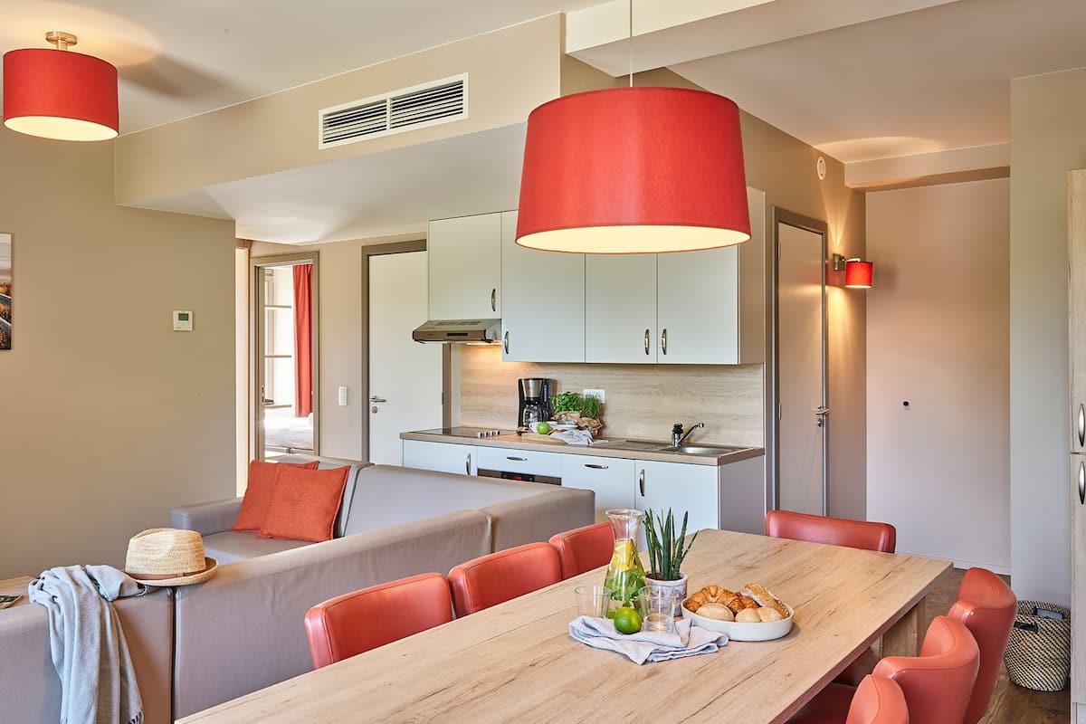Une cuisine moderne avec des meubles blancs, un plan de travail en bois et des suspensions rouges.