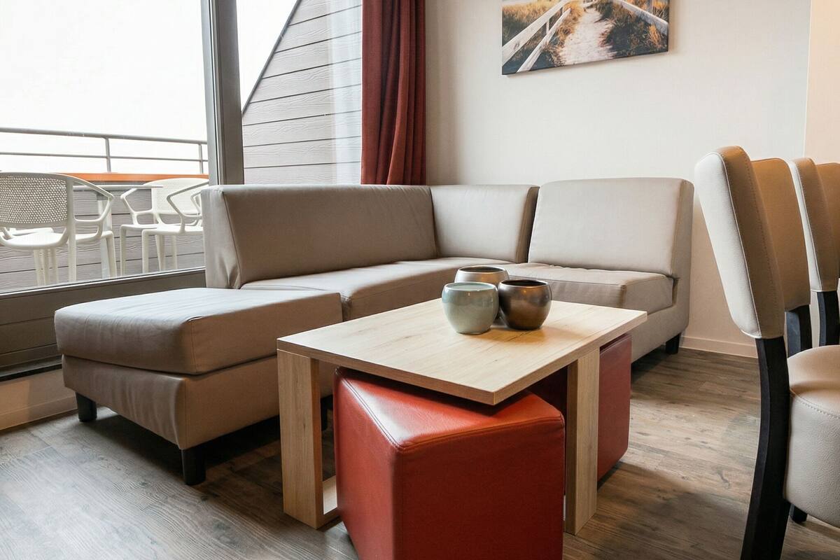 Un salon moderne avec un canapé d’angle, une petite table agrémentée d’objets décoratifs et un balcon équipé de mobilier d’extérieur.
