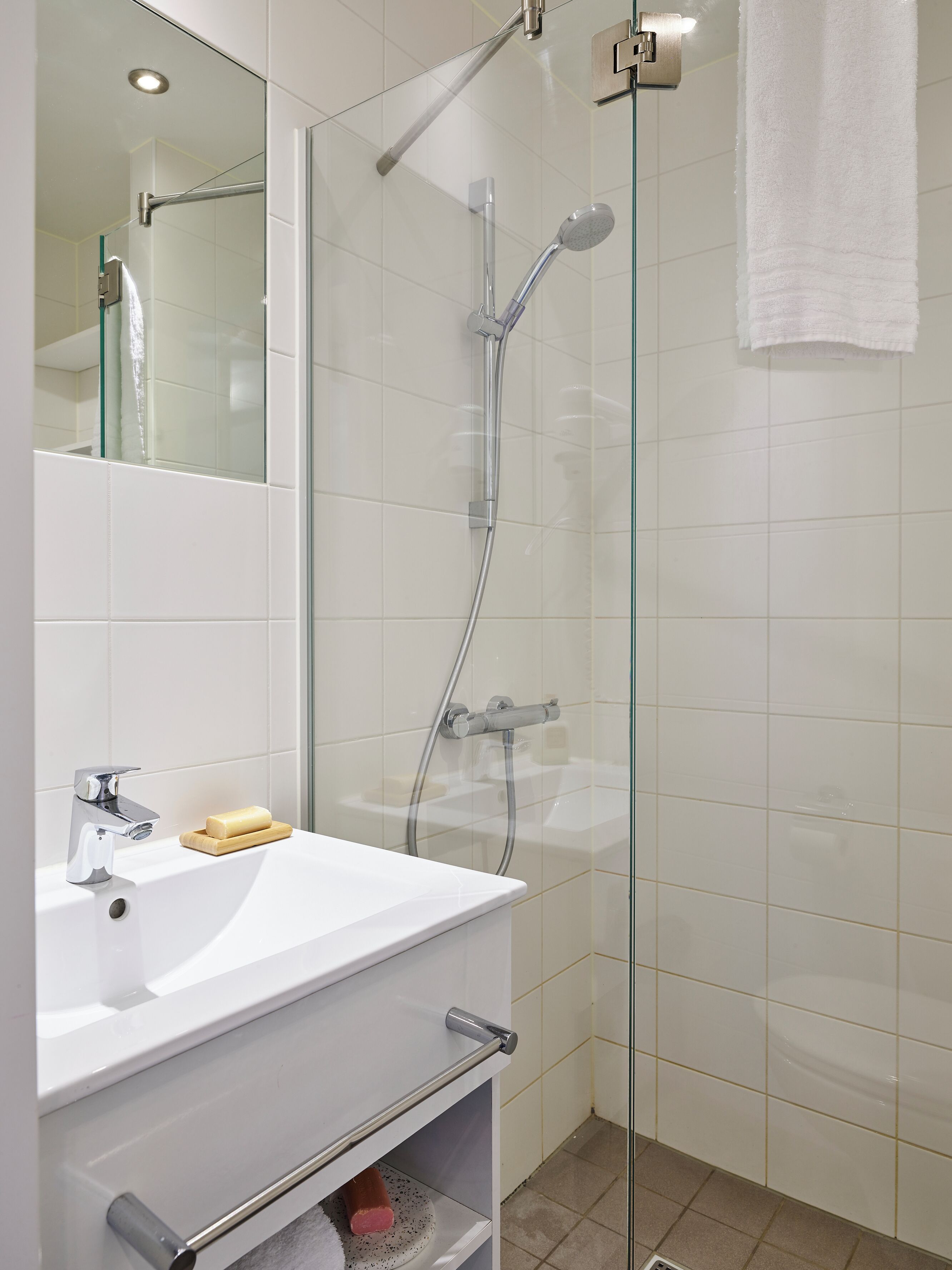 A modern bathroom with a glass shower enclosure, a white sink with a soap dish, and a mirror above the sink.