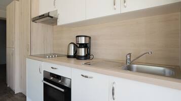 Een moderne keuken met witte kasten, een roestvrijstalen spoelbak, een koffiezetapparaat en een oven.