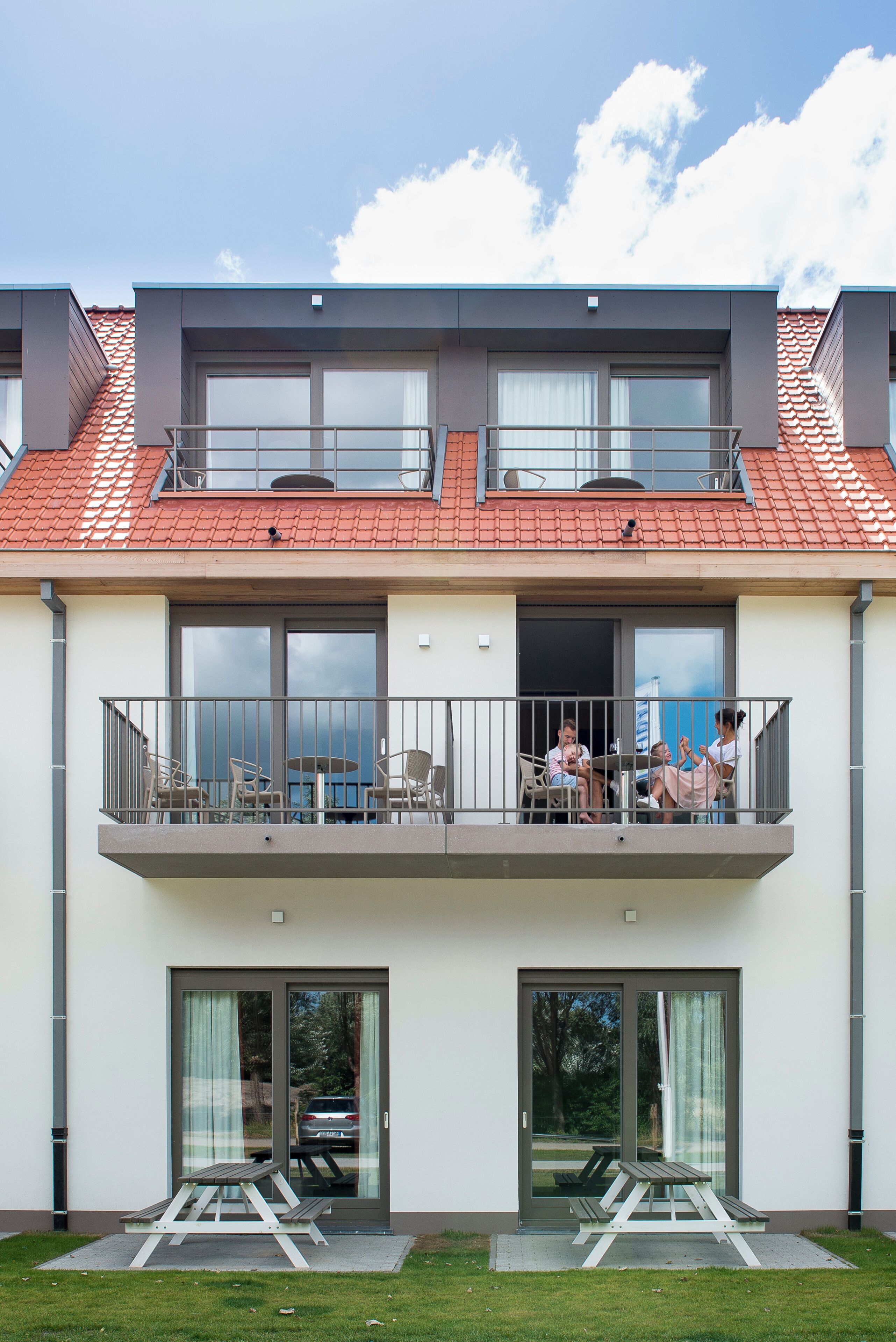 A two-story building with a balcony, large windows, and a red-tiled roof.