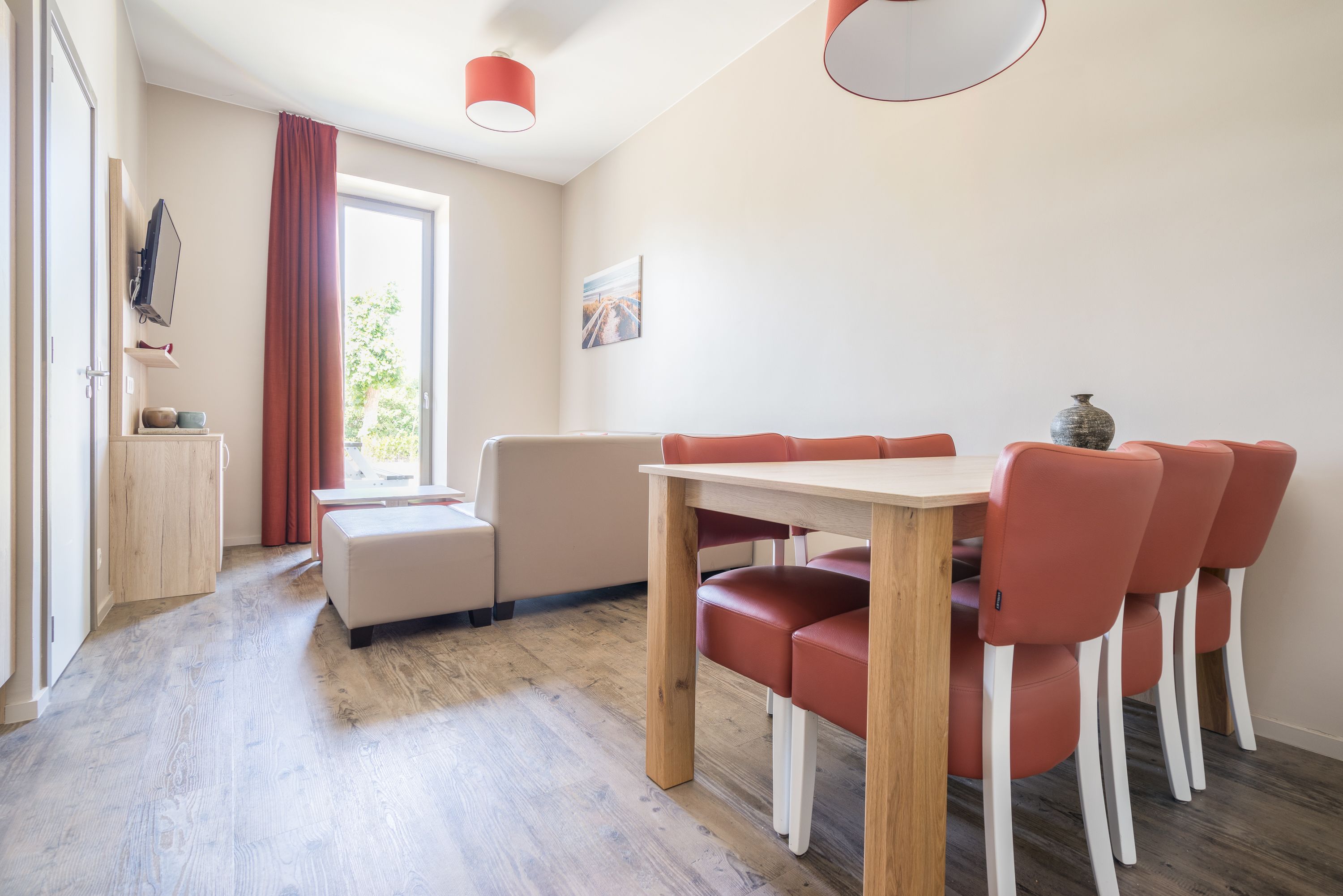 A modern dining area with a wooden table and red chairs, a bench, and a window with curtains.