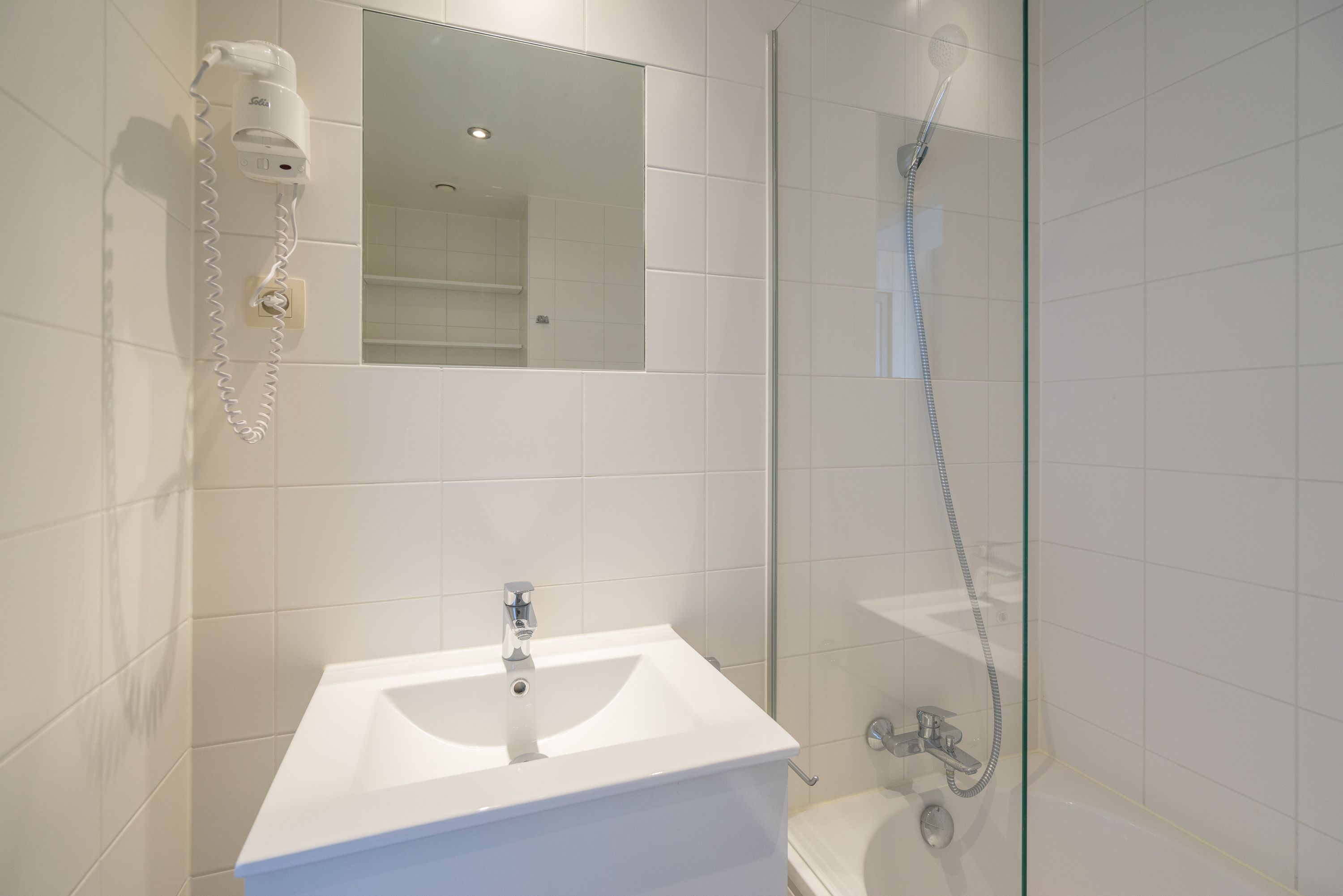 A modern bathroom with a white sink, a mirror, and a glass-enclosed shower.