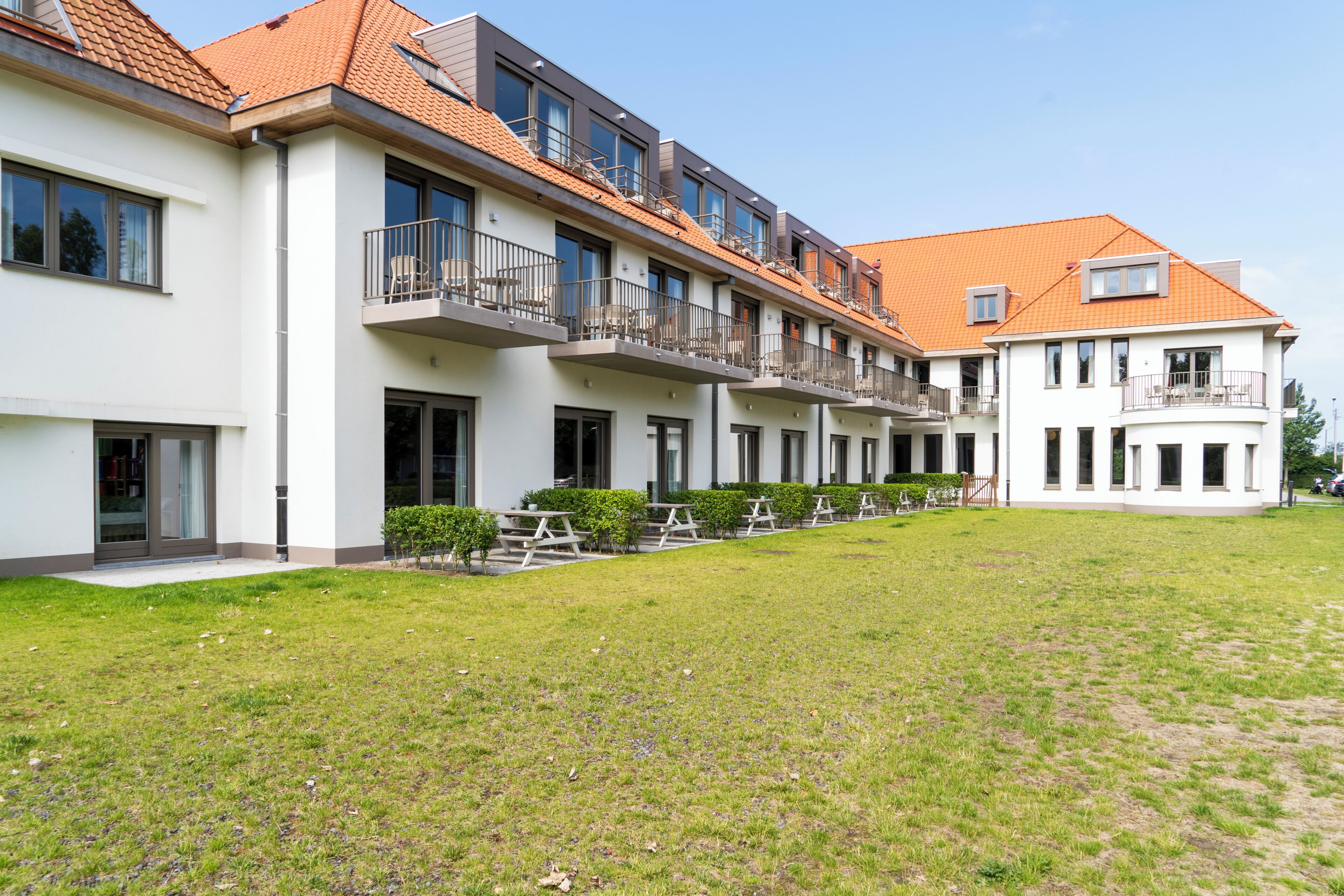 Une rangée d’immeubles modernes à plusieurs étages, dotés de balcons, un espace intérieur verdoyant et un ciel dégagé.
