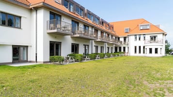 Une rangée d’immeubles modernes à plusieurs étages, dotés de balcons, un espace intérieur verdoyant et un ciel dégagé.