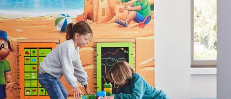 Dos niños jugando con bloques de construcción en una habitación con un mural de playa y una pizarra.