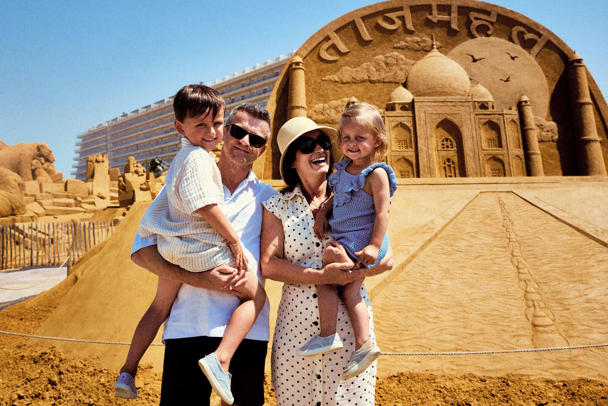 Une famille pose devant une grande sculpture de sable représentant un célèbre monument architectural.