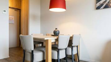 A dining area with a wooden table and chairs, a red pendant light, and a painting on the wall.