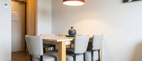 Un comedor con una mesa y sillas de madera, una lámpara colgante roja y un cuadro en la pared.