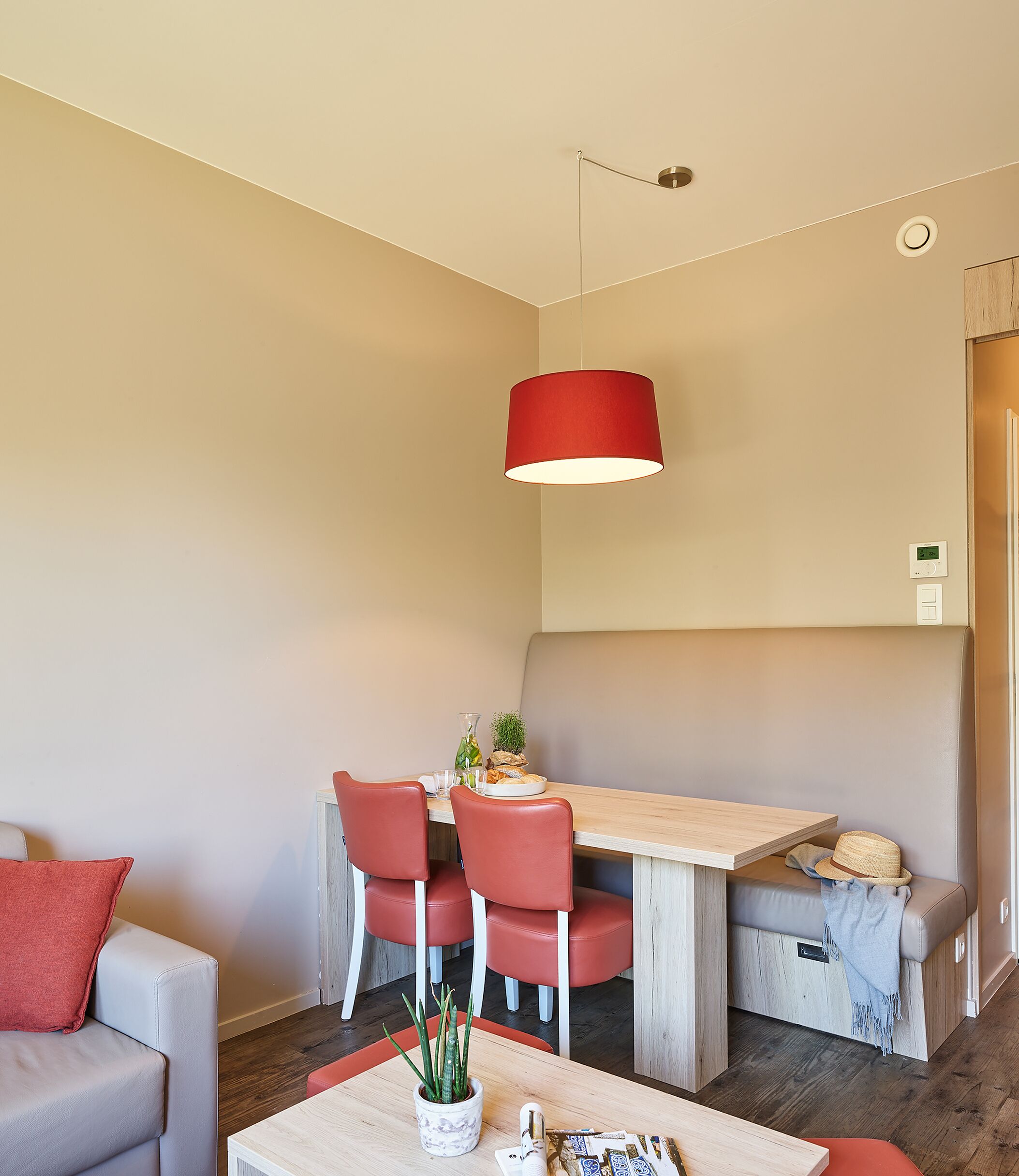 A compact living space with a dining area, a sofa, a table with a plant, and a red pendant light.
