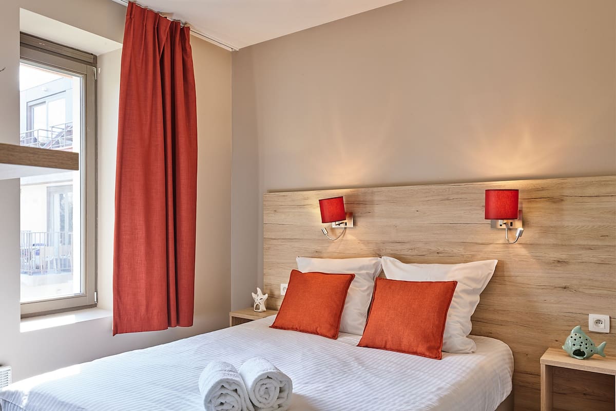 Une chambre d’hôtel avec un grand lit, deux lampes murales rouges et une fenêtre avec des rideaux rouges.