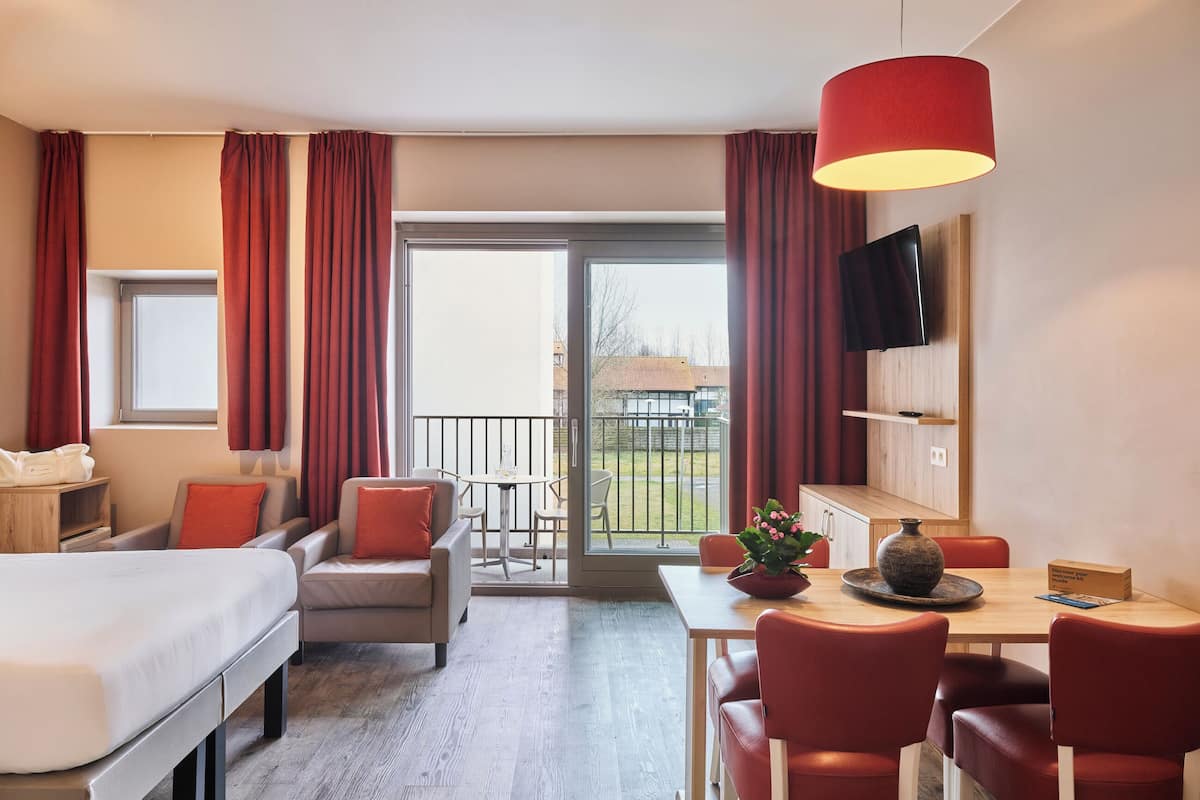 Une chambre d’hôtel comprenant un lit, un bureau avec des chaises, une table à manger et un balcon avec vue.