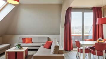 A modern living room with a grey sofa, red cushions, a wooden coffee table, and a dining area with a white table and red chairs.