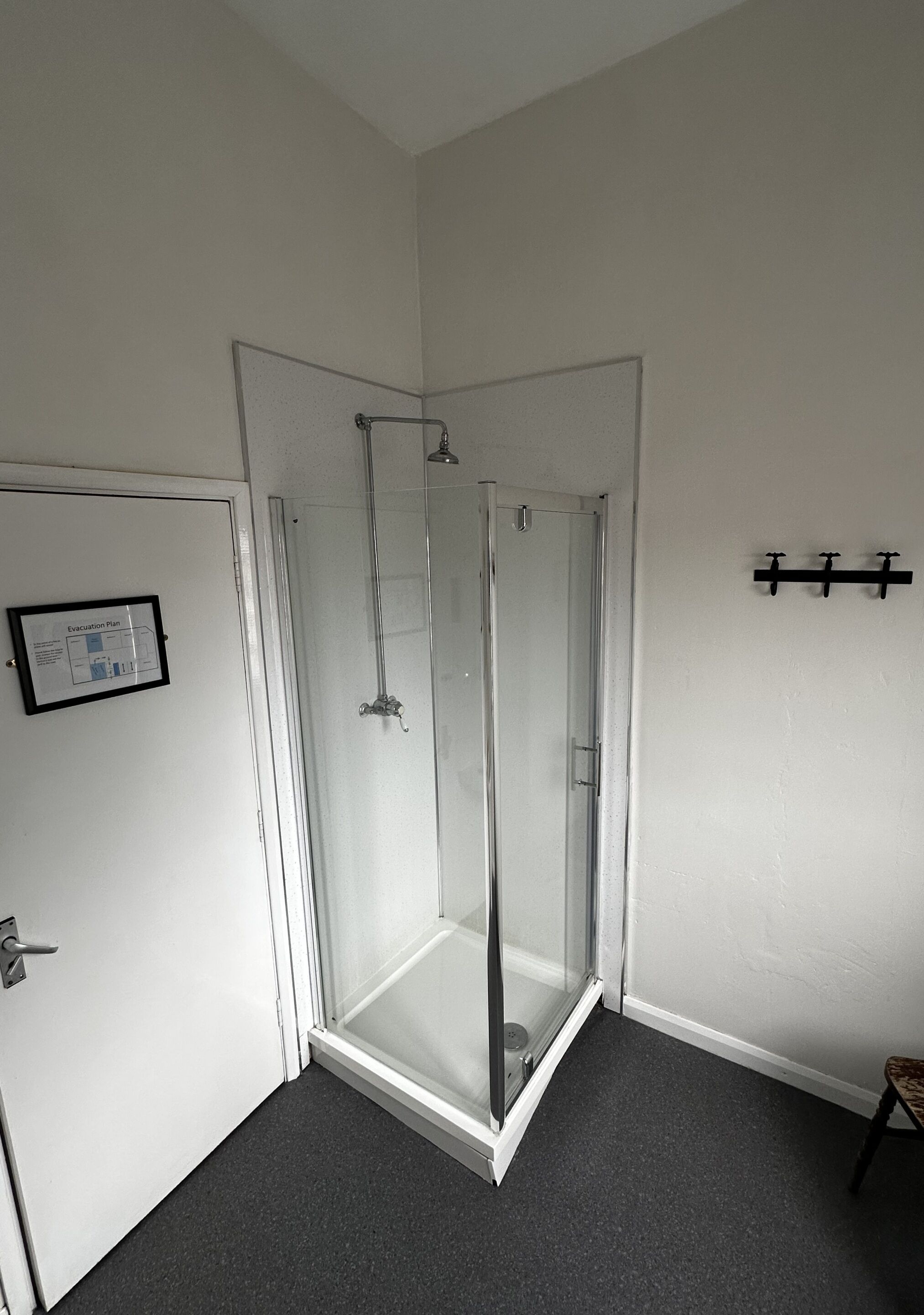 A corner shower with clear glass doors, a white door with a framed notice, and a small stool.