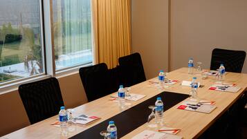A conference room with a long table, chairs, water bottles, name cards, and a window with a view of greenery.