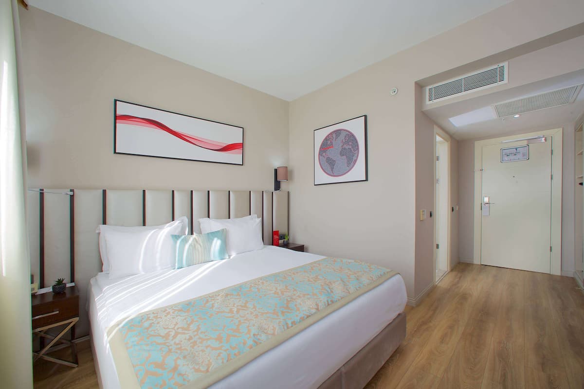 Une chambre d’hôtel avec un lit, une table de chevet, une lampe et une porte.
