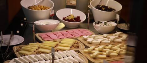 Buffet com diversos itens, incluindo queijos, carnes e frutas.