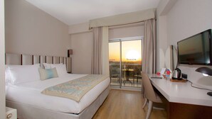 A hotel room with a bed, desk, chair, TV, and a view of the sunset through the window. - Ramada by Wyndham Soma (Soma)