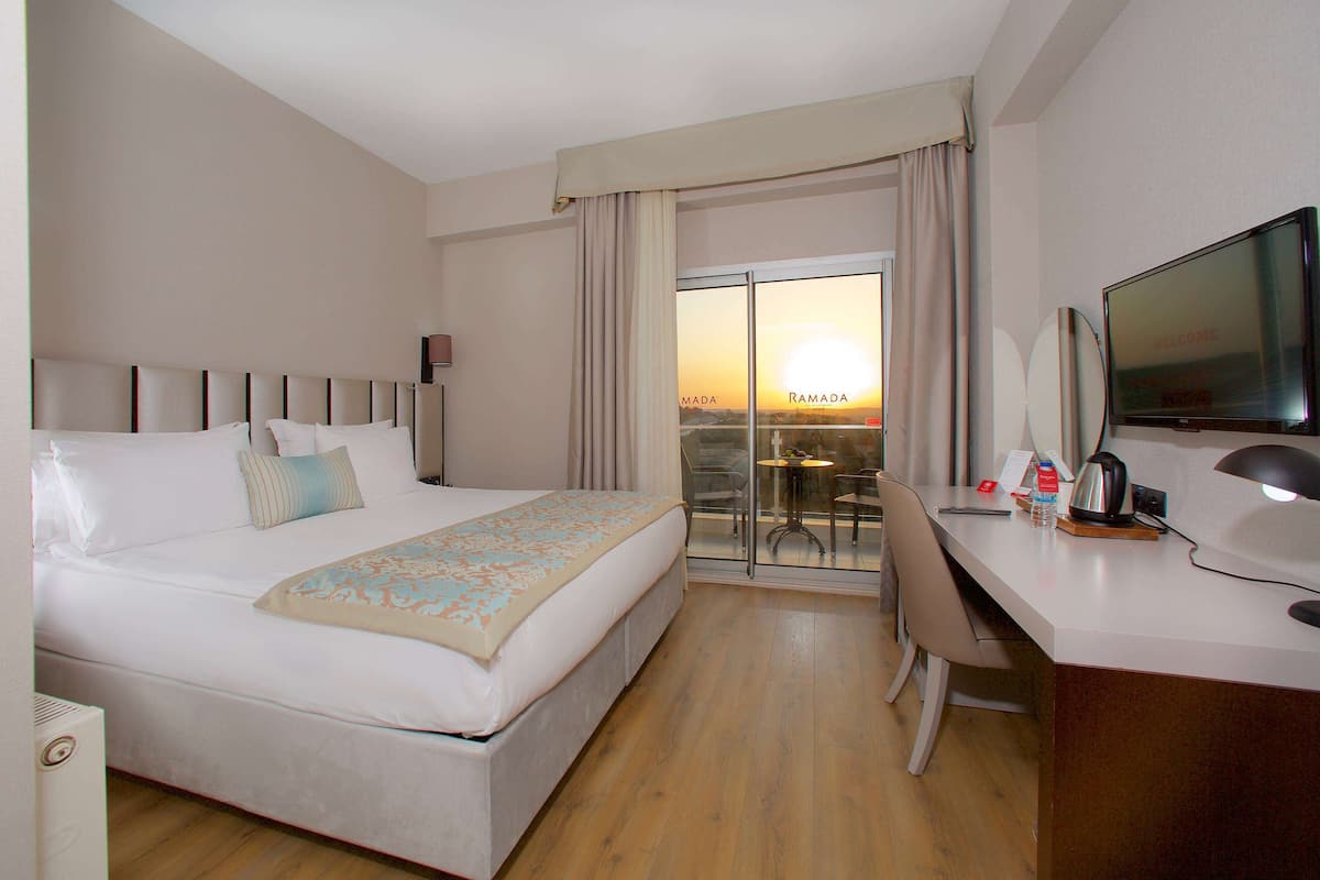 Une chambre d’hôtel équipée d’un lit, d’un bureau, d’une chaise, d’une télévision et offrant une vue sur le coucher de soleil par la fenêtre.