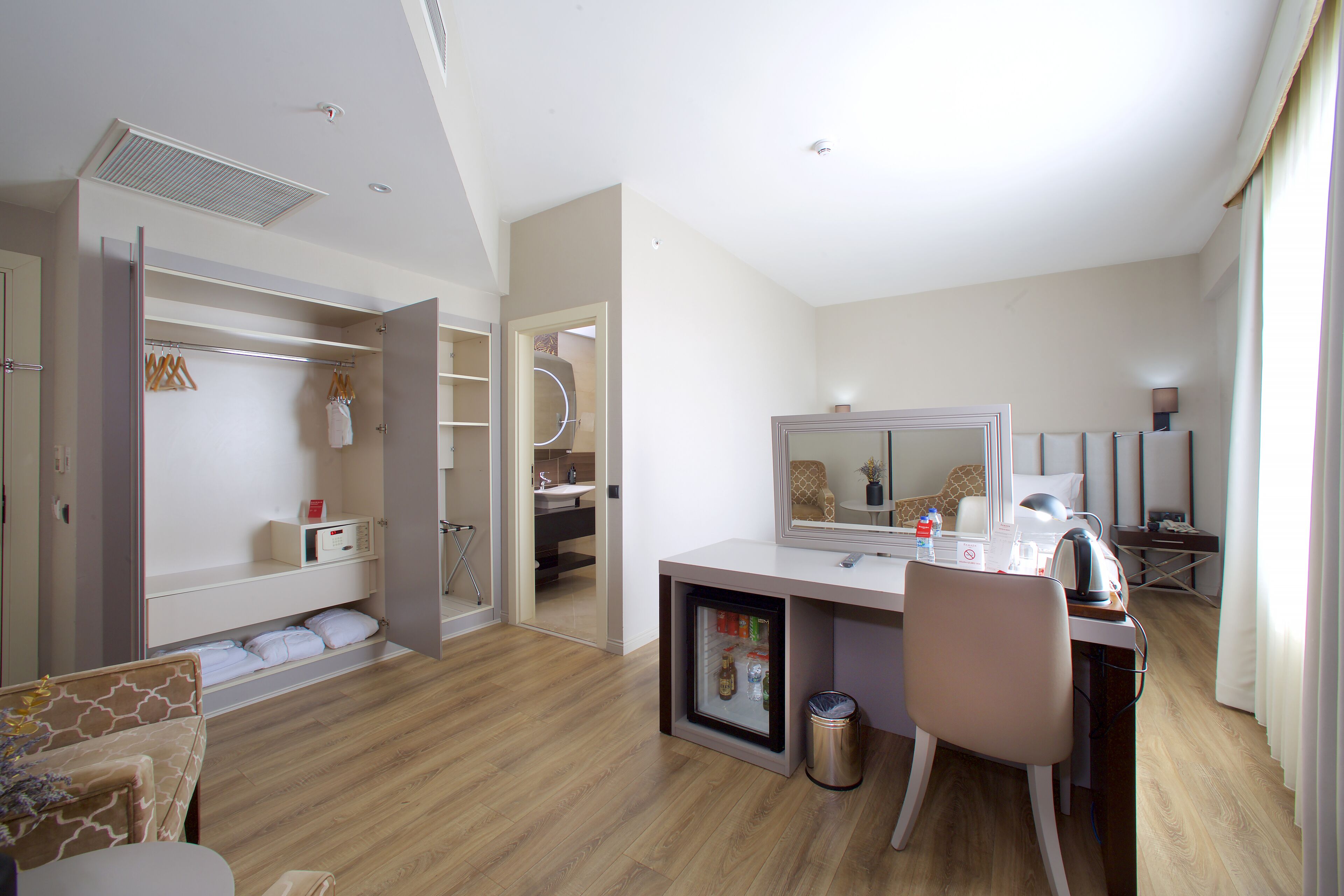 Una habitación de hotel moderna con cama, escritorio con computadora, espejo y armario.